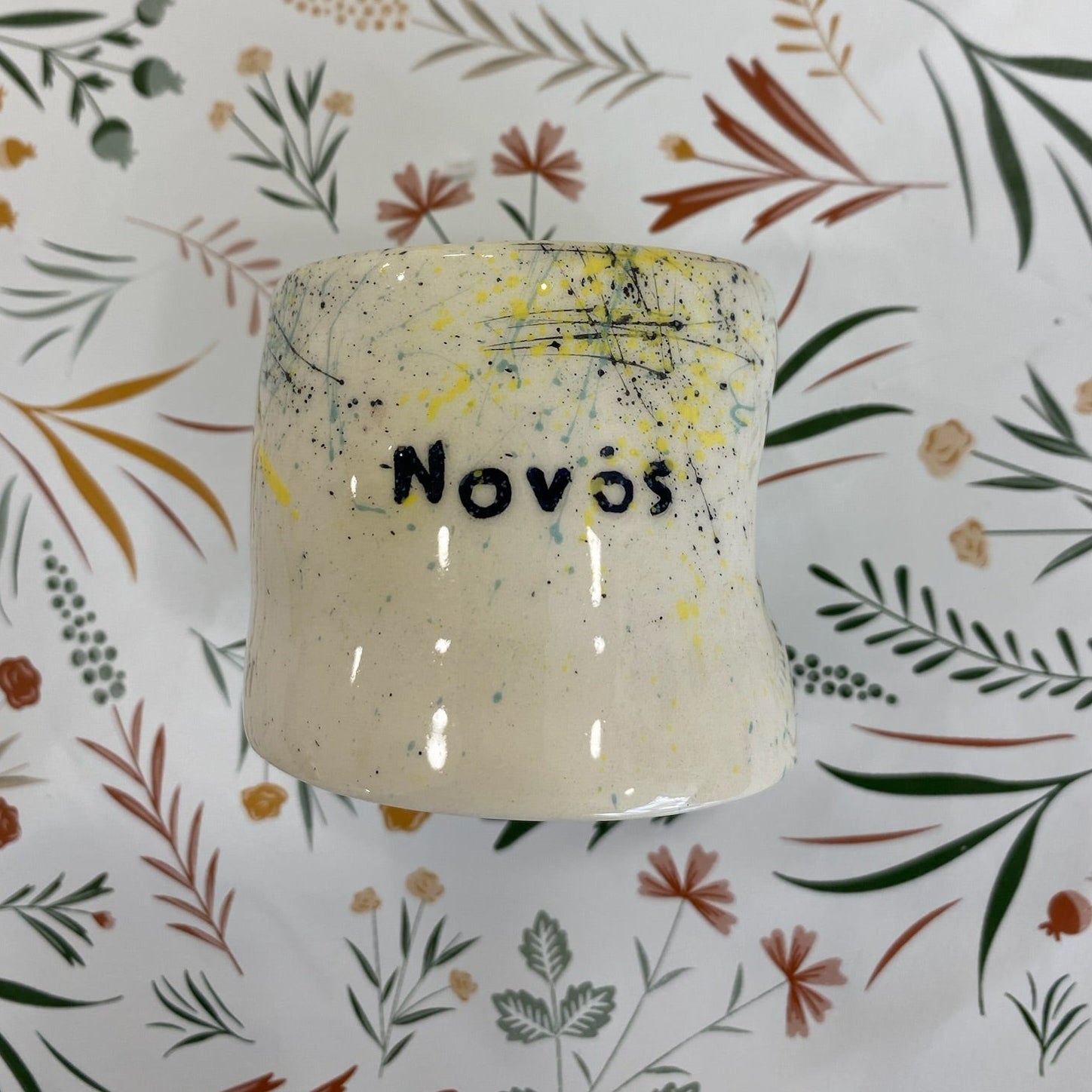 Ceramic container with 'Novos' saying on a floral-patterned background