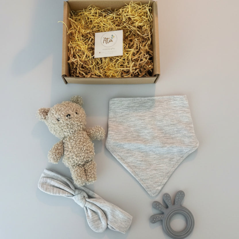 Baby items including a teddy bear a and teether on a surface. Detailed view of  the gift set .