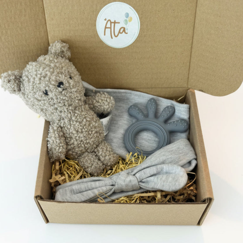 gift set with grey teddy bear and baby supplies inside a brandedbox on a grey background